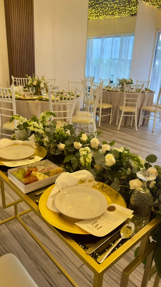 Mesa montada con mantelería dorada, vajilla y centros de flores blancas para una boda íntima en Merak Eventos