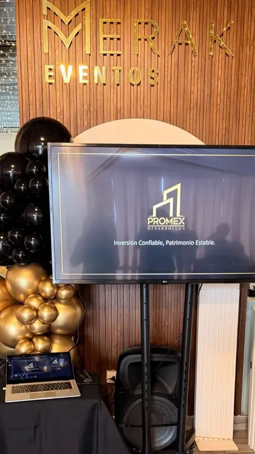 Pantalla de presentación con globos negros y dorados en un evento corporativo en Merak Eventos