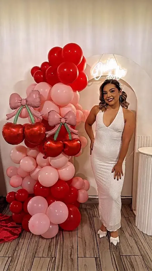 Festejada de blanco junto a un arco de globos en tonos rojo y rosa en una despedida de soltera en Merak Eventos