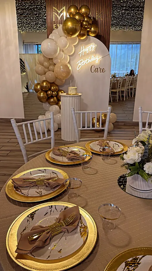 Arco de globos dorados, blancos y negros junto a la mesa montada para una celebración en Merak Eventos
